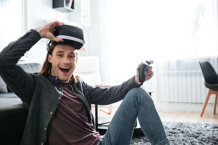 Young smiling man sitting at home indoors play games with PlayStation VR2. 